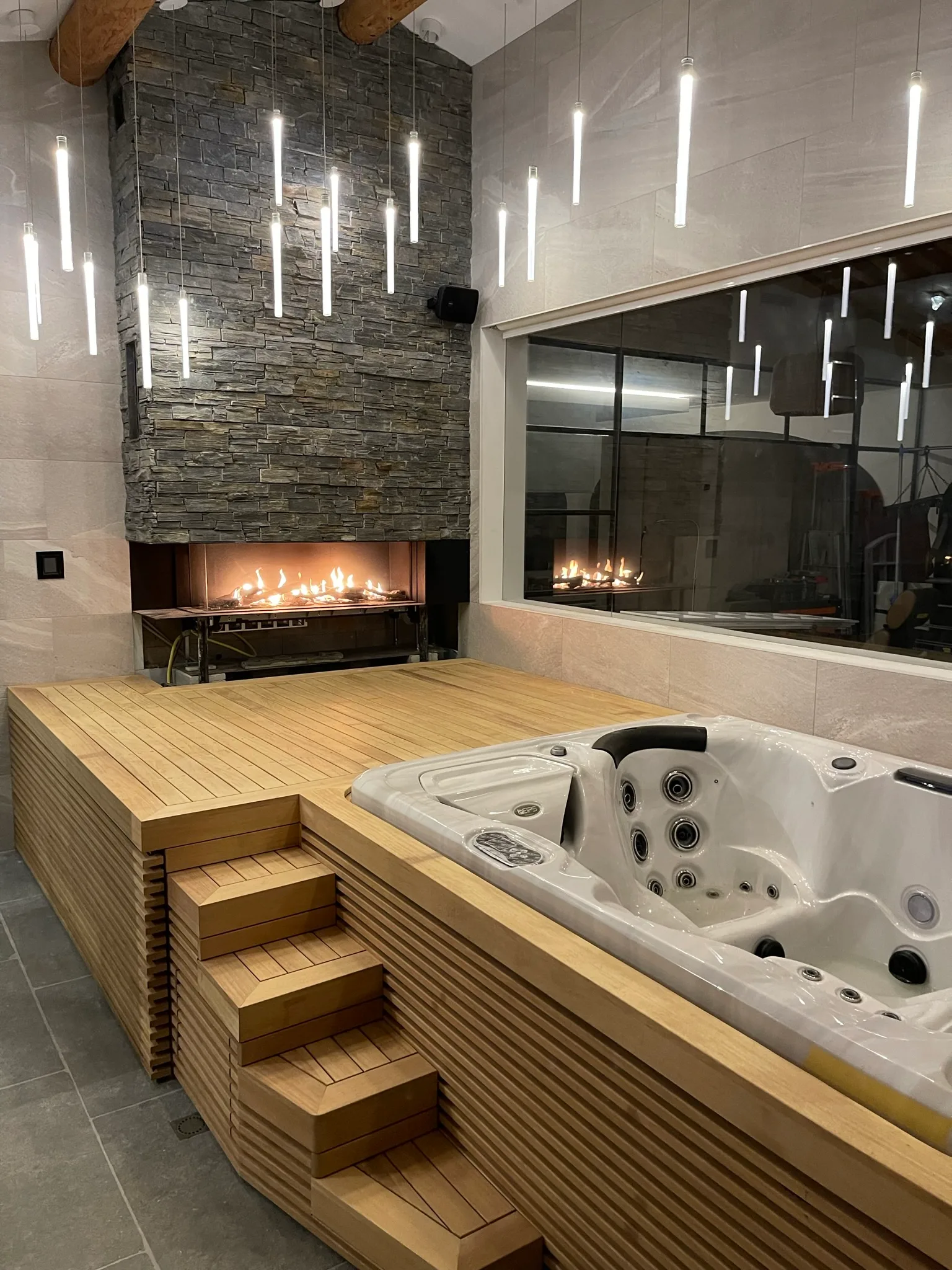 Espace bien-être avec jacuzzi, habillage en lamelles bois clair et cheminée pierre noire.
